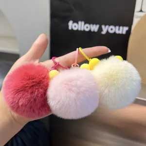 Close-up of soft faux rabbit fur pom pom keychains in pink and beige held by hand