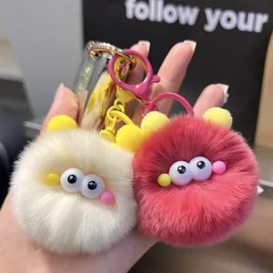 Close-up of cute plush pompom keychains in cream and rose red with soft faux fur detail
