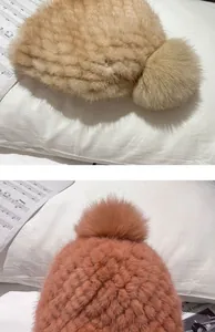 Close-up of woven mink fur hats with fluffy fox fur pom-poms in beige and reddish brown