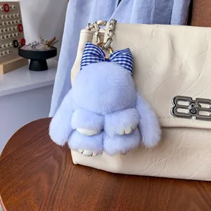 Dettaglio di un coniglio di peluche azzurro con fiocco appeso a una borsa di pelle beige