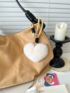 Detailopname van een witte hartvormige pluche sleutelhanger aan een kaki suède tas