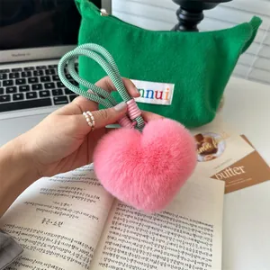 Detail van roze pluche hartvormige sleutelhanger met groen geweven touw aan tas