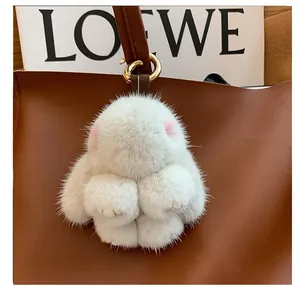 Close-up of white plush bunny keychain with gold hardware on a leather bag handle