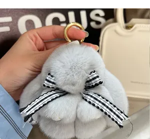Detail eines grauen Plüsch-Hasen-Schlüsselanhängers mit Karoschleife an einer Handtasche