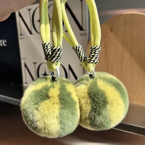 Detail of soft yellow and dark green rabbit fur pompom charms with yellow braided rope