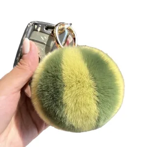 Striped rabbit fur pom-pom keychain in yellow and green with golden clasp on phone case