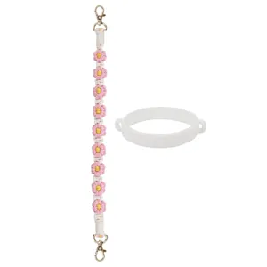 Détail d'une bandoulière tressée à fleurs rose et jaune avec fermoirs dorés et anneau silicone