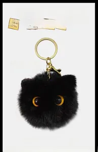 Close-up of black fluffy plush cat ball keychain with yellow eyes and gold metal hook