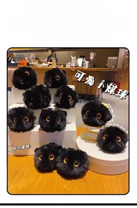 Close-up of fuzzy black soot sprite plush keychains with yellow eyes on a white display