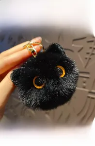 Close-up of black fuzzy cat plush keychain with big orange eyes and gold ring