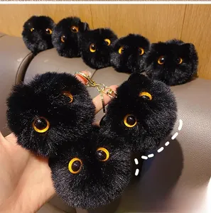 Close-up of black fuzzy coal ball plush keychain with orange eyes and gold metal chain
