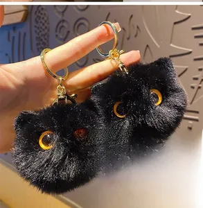 Close-up of two fluffy black plush cat ball keychains with big orange eyes and gold hardware
