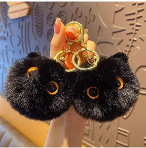 Macro view of fluffy black cat plush keychain with orange eyes and gold metal lobster clasp