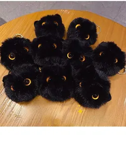 Close-up of cute black plush pompom keychain with big yellow eyes on wooden surface
