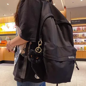 Minimalist black canvas backpack with a cute black fluffy plush cat ball keychain charm