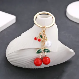 Detail of red cherry pendant keychain with white pearl on golden metal ring