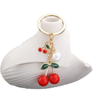 Golden cherry keychain with red enamel fruits and pearl detail on white background