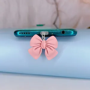 Détail d'un bouchon anti-poussière en forme de nœud rose sur un smartphone vert