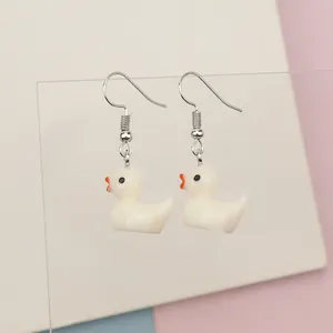 Detail of cute white resin duck earrings hanging on a transparent display stand