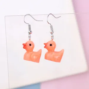 Close-up of orange-pink resin duck earrings with silver hooks on transparent display
