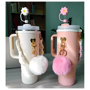 White and pink insulated tumblers with floral straw covers and fuzzy ball charms