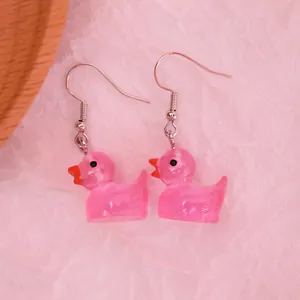 Macro detail of cute pink resin duck earrings with silver hooks on textured background