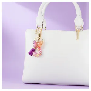 Détail du porte-clés lettre J en résine avec pompon violet, papillon et paillettes