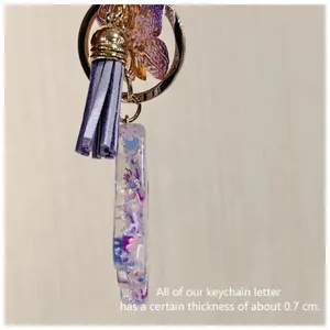 Handmade resin letter keychain with purple glitter, butterfly pendant, and tassel detail