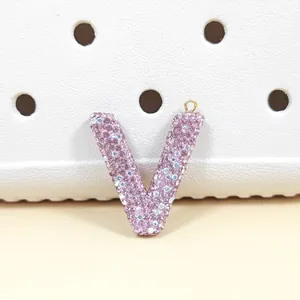 Vue macro d'un charm lettre V incrusté de strass roses sur une surface texturée