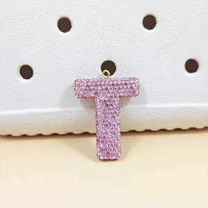 Charm lettre T en strass rose pour sabots présenté sur un fond blanc texturé à trous