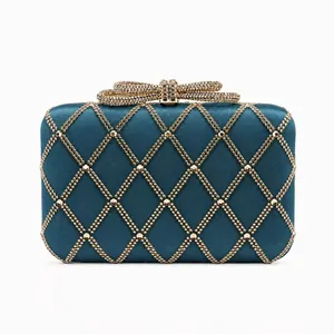 Macro detail of navy satin clutch with gold bead lattice and bow metal clasp