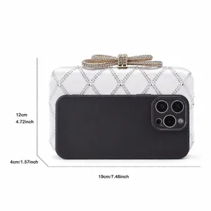 Detailed close-up of crystal bow clasp on white satin evening clutch bag with dimensions