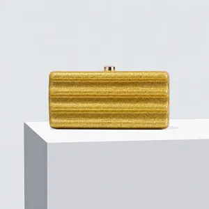Detail of glitter evening clutch bag with wave texture and gold clasp on white stand