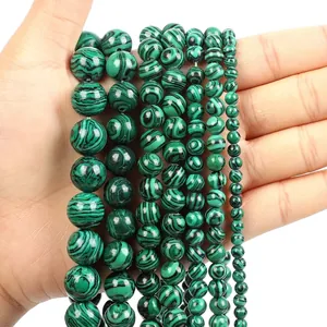 Macro detail of malachite style green beads in various sizes held by hand for comparison