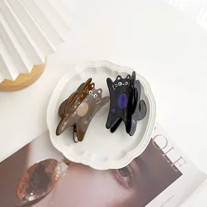 Détail de grandes pinces à cheveux chat en acétate marron et noir sur plateau blanc