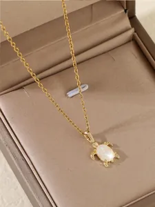 Détail d'un pendentif tortue dorée avec une carapace en opale sur chaîne croisée