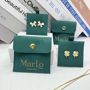 Detail of clover earrings and bow studs on dark green velvet jewelry pouches with gold logo