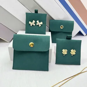 Detail of clover earrings and bow studs on dark green velvet jewelry pouches with gold logo