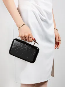 Close-up of black glossy evening clutch with textured finish and gold branch-like handle