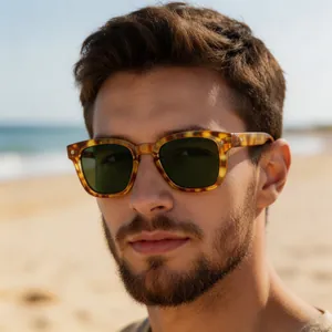 Close-up of tortoise shell sunglasses with green lenses worn by a model on a sunny beach