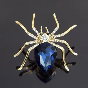 Detailed close-up of golden spider brooch with deep blue teardrop gemstone and crystals
