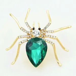 Close-up of golden spider brooch with a pear-cut green gemstone and sparkling crystals