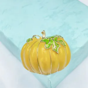 Close-up of yellow enamel pumpkin brooch with green leaves on a light blue gift box