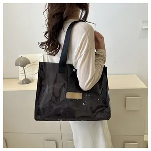 Detailed side view of large transparent PVC tote bag with black strap and leather logo tag