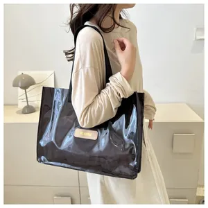 Detail of glossy black patent leather tote bag with a beige brand label and shoulder strap