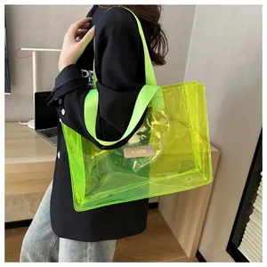 Detail of transparent PVC tote bag with neon green handles and branded leather patch