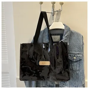 Close-up of black glossy PVC tote bag with leather logo patch and metal snap button