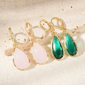 Elegant gold drop earrings with pink and emerald green stones on a stone background