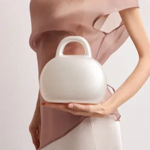 Detail shot of a minimalist pearl white acrylic evening bag with a sleek curved handle