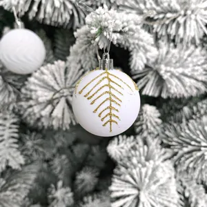 Détail de boule de Noël blanc mat avec motifs pailletés dorés sur des branches enneigées